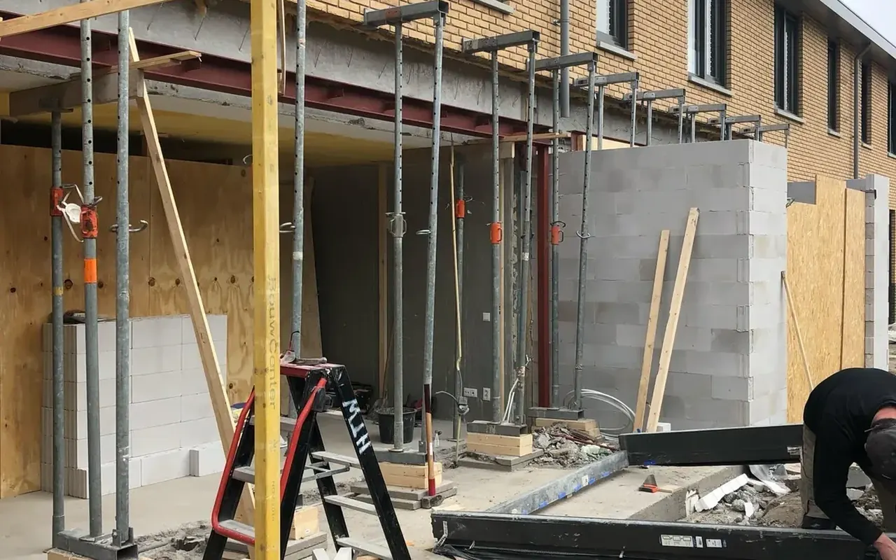 Aanbouw aan een rij woningen in de ruwbouw, met stempels, stalen ligger en kozijnprofiel op de bouwplaats